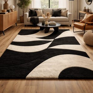 May include: A large, rectangular area rug with a bold, abstract design. The rug features a pattern of flowing, curved shapes in black and cream. The rug is placed on a hardwood floor in a living room setting.