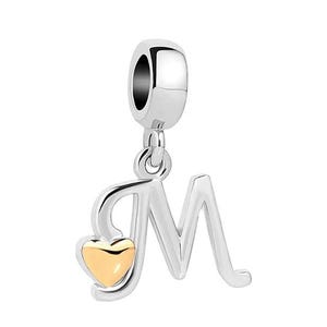 Puede incluir: Charm de plata con la letra "M" y un corazón dorado. El charm está diseñado para ser adjuntado a una pulsera o collar. El diseño es simple y elegante, adecuado para el uso diario.