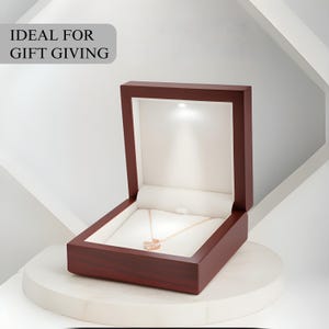 May include: A rose gold necklace with a pendant is displayed inside a dark wood jewelry box. The box is open, revealing a white interior and a small light. The text "IDEAL FOR GIFT GIVING" is in a gray box in the upper left corner.
