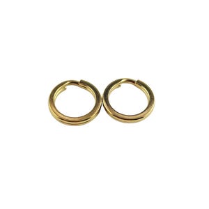 Op de afbeelding: Twee goudkleurige sleutelringen tegen een witte achtergrond. Elke ring is cirkelvormig met een spleet om sleutels aan te bevestigen. De ringen hebben een eenvoudig, klassiek ontwerp en lijken van metaal te zijn.