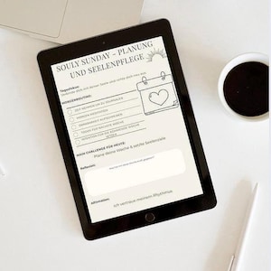 May include: A black tablet displaying a wellness planner with the text "SOULY SUNDAY - PLANUNG UND SEELENPFLEGE". The planner includes sections for journaling, meditation, and setting intentions. A cup of coffee, a pen, and a laptop are also visible.
