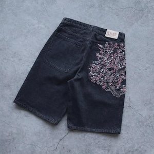 May include: Dark gray denim shorts with a floral embroidery design on the back pocket. The embroidery features pink and white flowers. The shorts have a classic five-pocket design and a button and zipper closure.