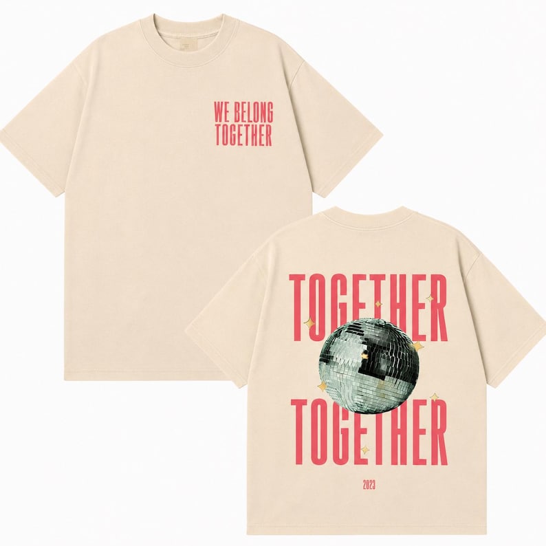 May include: Cream-colored t-shirt with short sleeves. The front features the text "WE BELONG TOGETHER" in red. The back displays the words "TOGETHER" twice, a disco ball graphic, and the year "2023" in red.