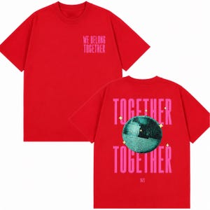 May include: Red t-shirt with the text "WE BELONG TOGETHER" in pink on the front. The back of the shirt features the words "TOGETHER" above and below a teal disco ball graphic, with the year "2023" below.