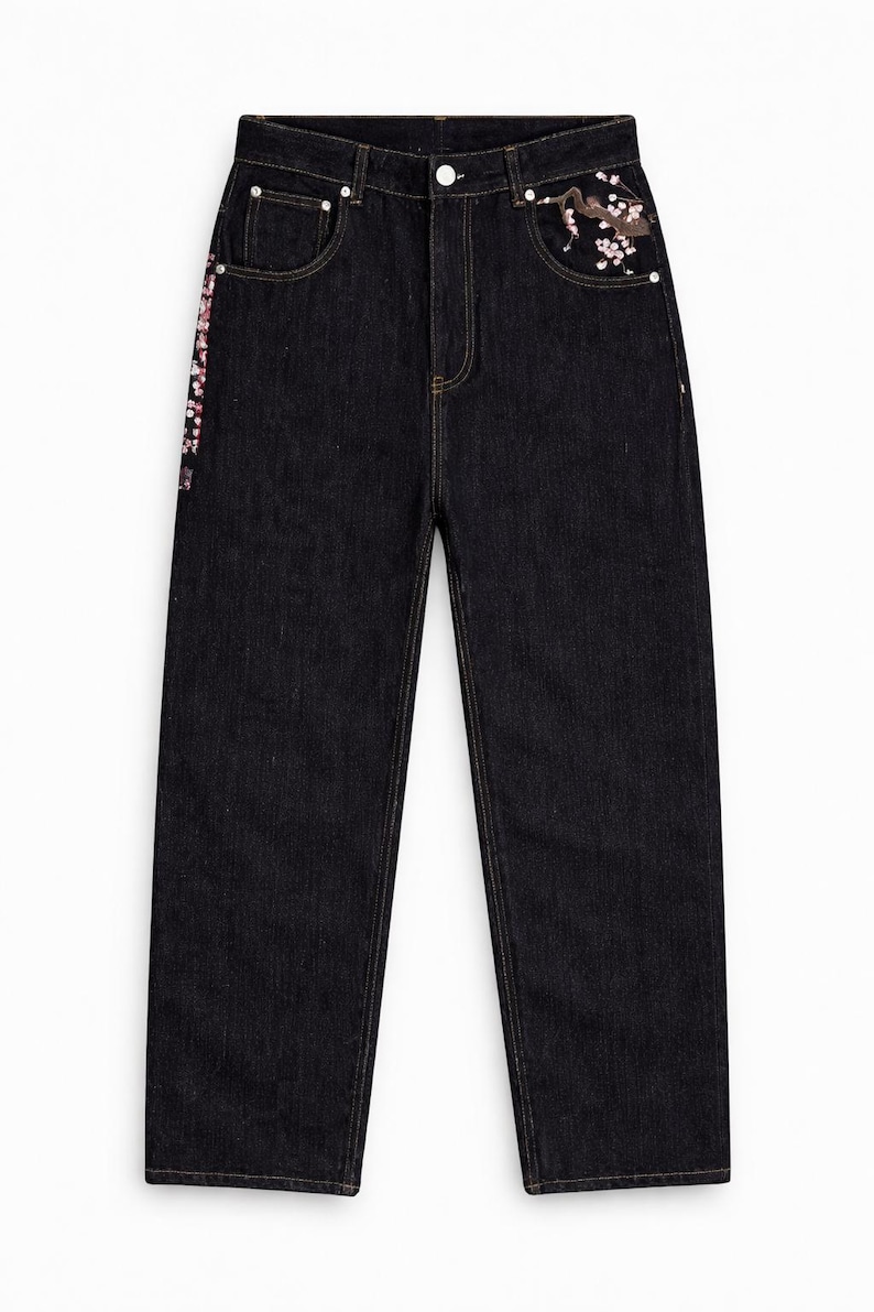 May include: Dark wash denim jeans with decorative floral embroidery on the front pocket and side seam. The jeans have a straight leg cut and classic five-pocket styling. The embroidery features pink and white flowers and a crane.