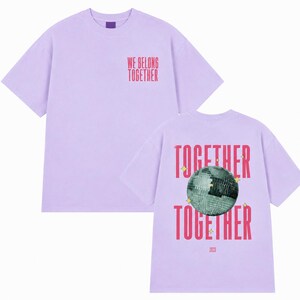 May include: Two light purple t-shirts. One displays the text "WE BELONG TOGETHER" in red. The other shirt has a disco ball graphic with the words "TOGETHER" above and below it, and the year "2023".