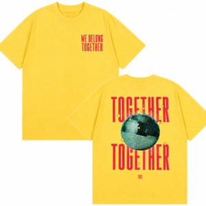 May include: Yellow t-shirt with red text that reads "WE BELONG TOGETHER" on the front and "TOGETHER" with a disco ball graphic on the back. The back also has the text "2023".