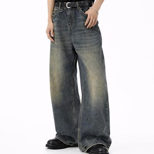 Op de afbeelding: Wijdvallende spijkerbroek van vervaagd blauw denim met een versleten afwerking. De broek heeft een hoge taille, een zwarte leren riem met een zilverkleurige gesp, een metalen D-ring aan de voorste riemlus en een klassiek ontwerp met vijf zakken.