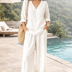 Peut inclure: Un ensemble deux pièces composé d'une tunique à manches longues blanc cassé avec un col en V et d'un pantalon assorti à jambes larges avec poches latérales. L'ensemble est accompagné d'un sac à bandoulière en paille tressée et d'une montre.