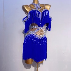 May include: A royal blue dance dress with fringe and sparkling embellishments. The dress features a halter-style neckline and off-the-shoulder sleeves, with a matching choker. The skirt is short and fringed, and the bodice is adorned with rhinestones.