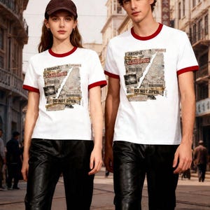 May include: Two people wearing white t-shirts with red trim and black leather pants. The shirts feature a graphic with the words "ARCHIVE", "CLASSIFIED", and "DO NOT OPEN". One person wears a brown baseball cap, the other a dark grey cap.