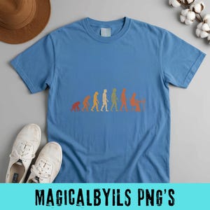 May include: A blue crew neck t-shirt featuring a multi-colored graphic print of human evolution, starting from a primate and progressing through various stages to a person sitting at a computer desk, displayed in a horizontal sequence.