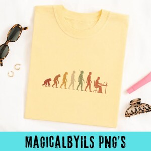 May include: A pale yellow t-shirt featuring a brown graphic print of human evolution, progressing from a primate to a person sitting at a desk with a laptop. The design is centered on the chest of the shirt, which is displayed flat.