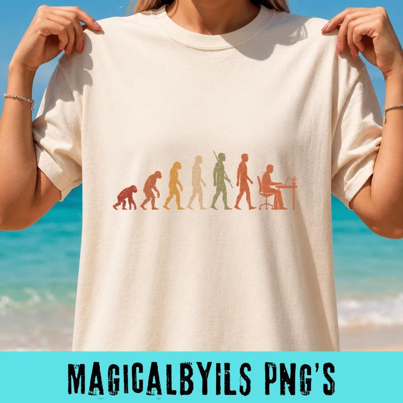 May include: A cream-colored short-sleeve t-shirt featuring a multi-colored graphic print of human evolution. The design shows a progression from a primate to a human sitting at a desk with a computer, rendered in shades of orange, yellow, and green.