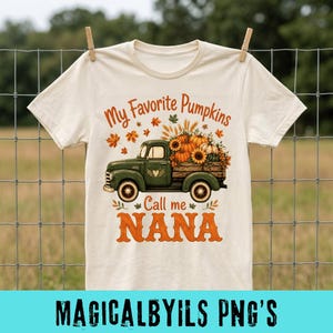 May include: A cream-colored short-sleeve t-shirt featuring a graphic of a green vintage truck carrying pumpkins and sunflowers. The text reads My Favorite Pumpkins Call me NANA in orange and brown lettering, surrounded by autumn leaves.