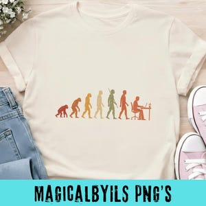 May include: A cream-colored short-sleeve t-shirt featuring a graphic print of human evolution in shades of orange and green. The design depicts the progression from a primate to a human sitting at a desk working on a laptop computer.