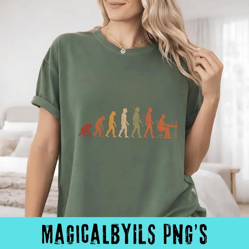 May include: An olive green short-sleeve t-shirt featuring a graphic print of the evolution of humanity, progressing from a primate to a human sitting at a desk with a computer. The design uses a gradient of orange, yellow, and green tones.