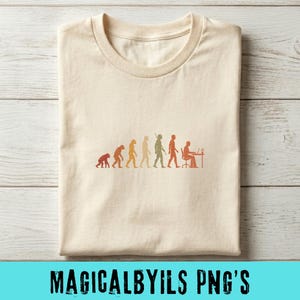 May include: A cream-colored t-shirt featuring a graphic print of the human evolution sequence. The design shows the progression from a primate to a modern human sitting at a desk with a computer, rendered in a gradient of orange and brown tones.