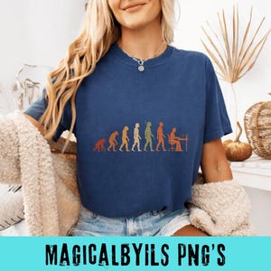 May include: A dark blue short-sleeve t-shirt featuring a graphic print of human evolution, starting with a primate and progressing through various stages to a person sitting at a desk with a computer, rendered in shades of orange, green, and yellow.