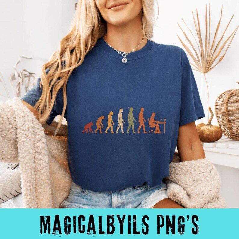 May include: A dark blue short-sleeve t-shirt featuring a graphic print of human evolution, starting with a primate and progressing through various stages to a person sitting at a desk with a computer, rendered in shades of orange, green, and yellow.
