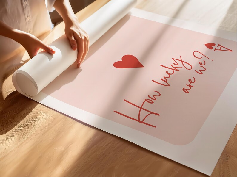 May include: A rolled-up poster with the text "How lucky are we?" in red script, along with a red heart and a playing card symbol. The poster is on a light pink background.
