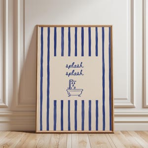 May include: A rectangular framed wall art piece featuring a beige background with vertical dark blue stripes along the top and bottom edges. The center displays the text "splash splash" in blue script above a blue line drawing of a bathtub.