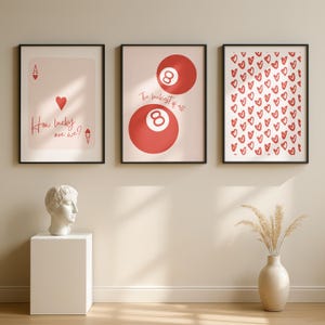 May include: Three framed art prints with black frames. One print features a playing card with a heart and the text "How lucky are we?". Another shows two red 8-balls with the text "The luckiest of all". The third print has a pattern of red hearts.