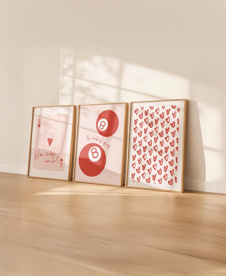 May include: Three framed art prints with a light wood frame. The prints feature a playing card, a red eight ball, and a pattern of red hearts. Text on the prints reads "How lucky are we?" and "The luckiest of all."