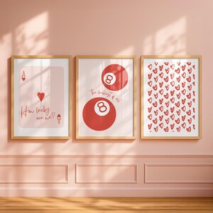 May include: Three framed art prints with a light wood finish. The left print features a playing card design with the text "How lucky are we?". The center print shows two red 8-balls with the text "The luckiest of all". The right print is covered in red hearts.