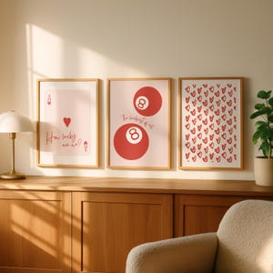 May include: Three framed art prints with a light wood finish. The prints feature a playing card design, a pair of red 8-balls, and a pattern of red hearts. Text on the prints reads "How lucky are we?" and "The luckiest of all."