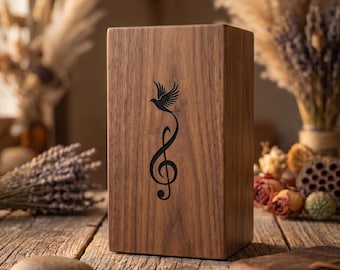 Puede incluir: Una caja de madera rectangular con acabado marrón oscuro. En la parte delantera, una ilustración negra de un pájaro y una nota musical. La caja está sobre una superficie de madera.