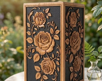 Puede incluir: Una caja de madera rectangular con intrincadas tallas de rosas y hojas. La caja tiene un panel central gris oscuro enmarcado por madera marrón claro. El diseño floral es de un marrón más claro. La caja está sobre una mesa de mármol.