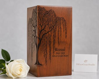 May include: A rectangular brown wooden urn featuring a laser-engraved willow tree design on the front. The text reads Rossi, 2018-2025, and Always in our Hearts. A single white rose is positioned to the left, and a small white card reads ISEverGraceStudio.