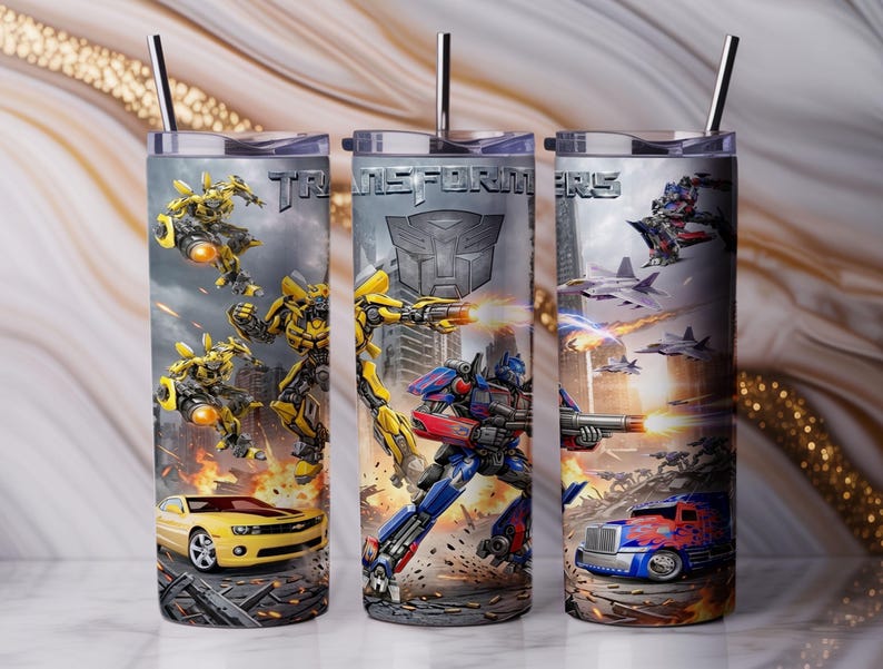 May include: Three cylindrical tumblers with metal straws featuring Transformers graphics. The designs include yellow and blue robot characters, a yellow sports car, a blue truck, fighter jets, and the Transformers logo printed in silver metallic lettering.