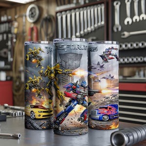 May include: Three cylindrical tumblers featuring Transformers graphics, including Bumblebee in yellow car and robot forms, Optimus Prime in blue truck and robot forms, the Autobot logo, and the Transformers text logo against a battle-themed background.