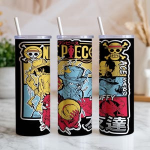 May include: Three cylindrical tumblers with white straws, featuring a black background and colorful anime-style graphics. The designs include the text "ONE PIECE," "ACE," "SABO," and "LUFFY," alongside illustrations of characters wearing hats and various Japanese characters.