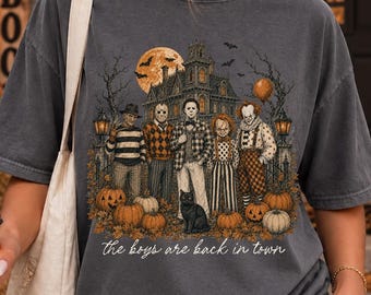 May include: A charcoal gray t-shirt featuring a graphic print of five horror movie characters standing in front of a haunted house with pumpkins, a black cat, and a full moon. The text "the boys are back in town" is printed in white script below.