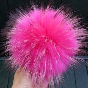 May include: A bright pink fur pom-pom. The fluffy accessory is round and has long, soft, and textured fur. The pom-pom is a vivid, eye-catching colour, perfect for adding a pop of colour to any project.