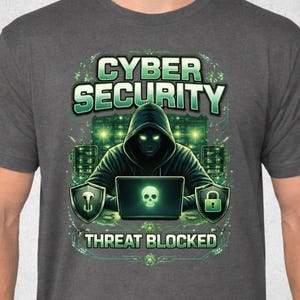 Könnte beinhalten: Graues T-Shirt mit einem Grafikdesign zum Thema Cybersicherheit. Das Design enthält die Worte "CYBER SECURITY" über einer Illustration einer Kapuzenfigur, die einen Laptop mit einem Totenkopf auf dem Bildschirm benutzt. Der Text "THREAT BLOCKED" steht darunter.