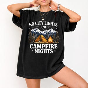 May include: Black t-shirt with a camping graphic. The design features a tent, campfire, mountains, and the text "NO CITY LIGHTS JUST CAMPFIRE NIGHTS". The shirt is a relaxed fit.