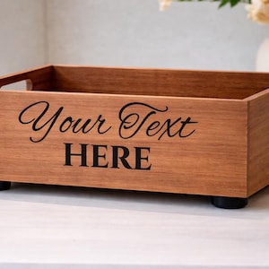 May include: A rectangular wooden tray with a natural finish. The tray has cut-out handles and sits on four black feet. The words "Your Text HERE" are printed on the front in black script and block letters. A decorative item.