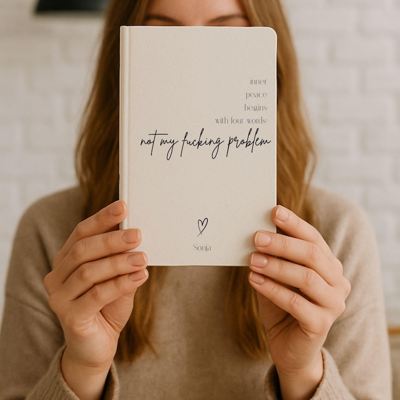 Puede incluir: Un cuaderno color crema con el texto "inner peace begins with four words: not my fucking problem." Un peque&ntilde;o coraz&oacute;n y el nombre "Sonja" est&aacute;n debajo. El cuaderno est&aacute; sostenido frente a una persona.