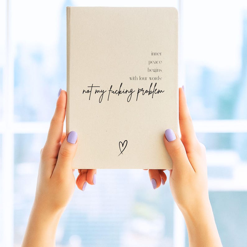 Puede incluir: Un cuaderno color crema sostenido por manos con esmalte de u&ntilde;as lavanda. El cuaderno presenta el texto "inner peace begins with four words: not my fucking problem" y un peque&ntilde;o s&iacute;mbolo de coraz&oacute;n.