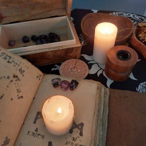 May include: A wooden box with amethyst stones, a lit candle, and an open book with symbols. A white candle and incense burner are also present, suggesting a spiritual or mystical theme.