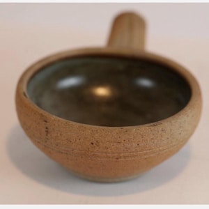 May include: A set of three ceramic mugs with a speckled, matte finish. The mugs are in shades of cream, light gray, and dark gray. Each mug has a simple, minimalist design and a rounded handle. The mugs are likely for coffee or tea.