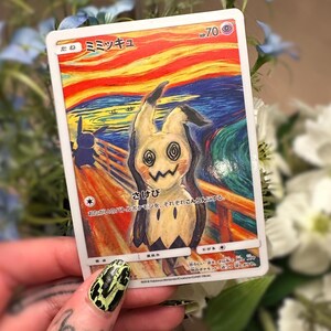 May include: A Mimikyu Pok&eacute;mon trading card with a distinctive artistic design. The card depicts a Mimikyu character in the style of Edvard Munch's "The Scream". The card includes Japanese text and a HP of 70.