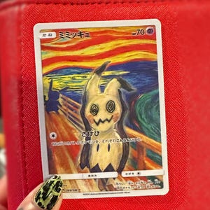 May include: A Pok&eacute;mon trading card depicting Mimikyu in a parody of Edvard Munch's "The Scream." The card has Japanese text and a colourful background with a figure on a bridge. The card is held against a red background.