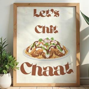 May include: A framed print with the words "Let's Chit Chaat" in brown lettering. The image features a colorful illustration of a plate of chaat, a popular Indian street food, with various toppings. The frame is made of light-coloured wood.