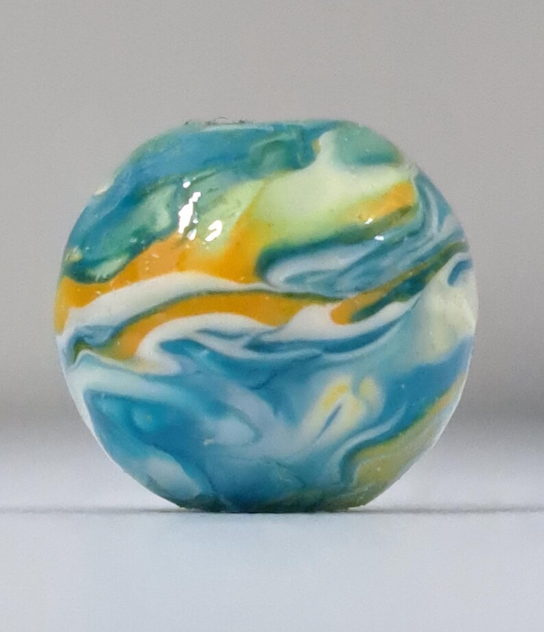 May include: A round, colorful bead with a marbled design. The bead features swirls of blue, yellow, white, and orange. The bead is a decorative element, possibly for jewelry or crafts.