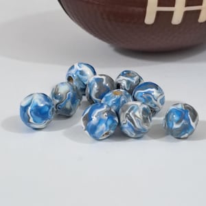May include: A collection of marbled beads in shades of blue, white, and gray. The beads have a glossy finish and a swirled pattern. A brown football is partially visible in the background.